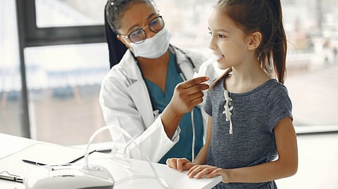 A doctor checks a smiling young girl with a stethoscope in a clinic.