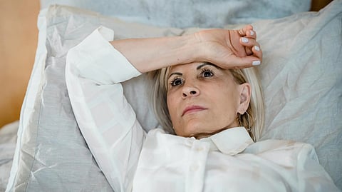 A woman lies on a bed with a pensive expression, her arm resting on her forehead.