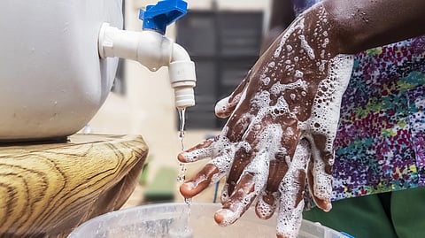 A person washes hands with soap under a faucet, water flowing into a bucket. 