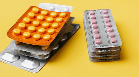 Stacks of blister packs containing yellow and pink pills on a bright yellow background. 