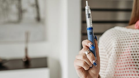 A person holds a blue insulin pen in their right hand, showcasing vibrant blue nail art. 