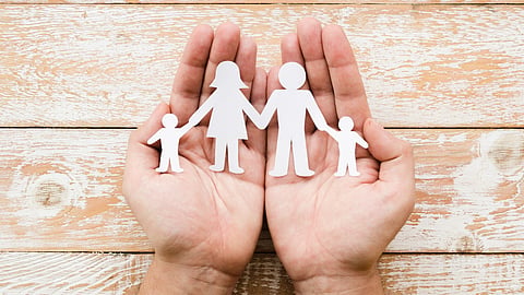 Hands holding paper family cutouts on a wooden background.