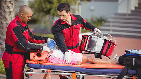 Two paramedics in red uniforms attend to an injured person on a stretcher.