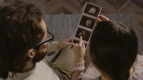 A couple sits closely, looking fondly at ultrasound images of 
