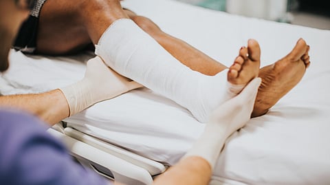 A healthcare worker in gloves gently supports a patient's leg, wrapped in a white bandage, while on a hospital bed.