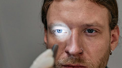 A gloved person holds a flashlight to a man's eye during an examination.