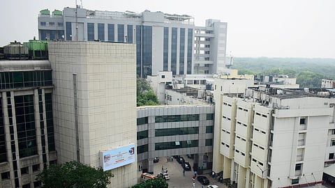 Aerial view of a modern hospital complex with several multi-story buildings surrounded by greenery, cars, and people.