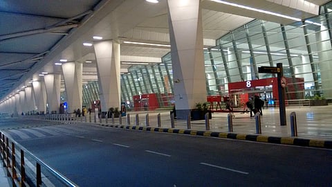 Spacious airport terminal entrance with towering columns, glass walls, and a road lined with barriers. 