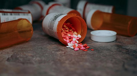 Open prescription pill bottle spilling colorful heart-shaped tablets on a dark surface.