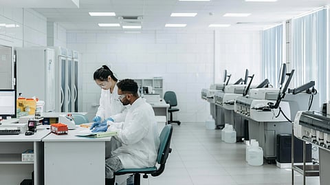 Two scientists in lab coats work at a laboratory desk.