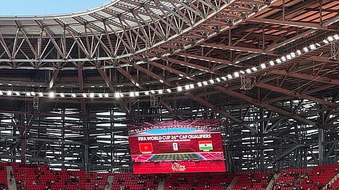 A large stadium with red seats and a digital screen showing FIFA World Cup 26 qualifiers.