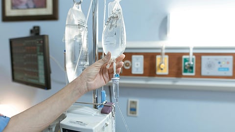 A hand adjusts an IV drip in a hospital room.