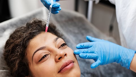 A woman receives a facial injection from a professional wearing blue gloves.