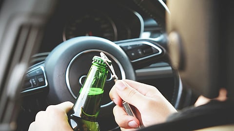 A person in a car opens a beer bottle with a key, showing unsafe drinking and driving behavior.