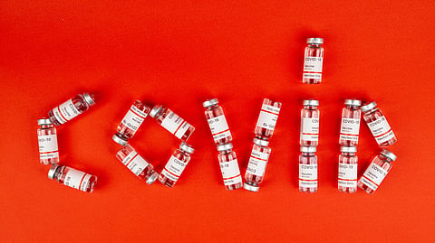 Vaccine vials arranged to spell “COVID” on an orange background, highlighting COVID-19 vaccination.