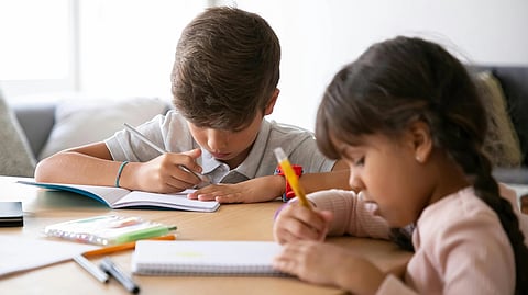 Two children focus intently on their homework at a wooden table.