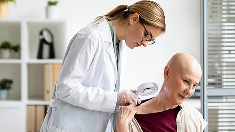 A female doctor examines a patient’s shoulder with a magnifying tool in a bright office.