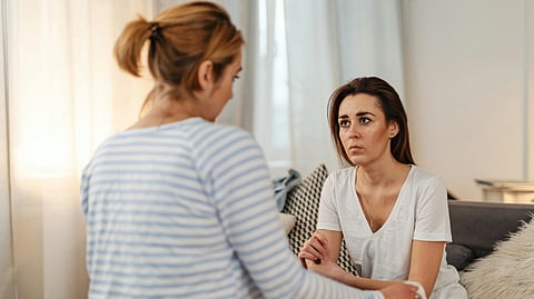 A woman converses with another woman while seated on a couch.