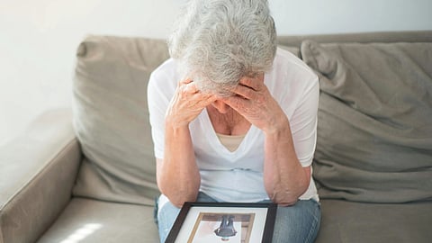 An older woman sitting on a couch, holding her head.