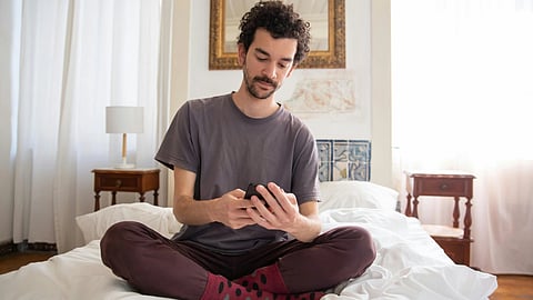 A man sitting on a bed, focused on his phone.