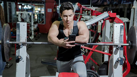 A man sits on a gym bench, focused on his phone.