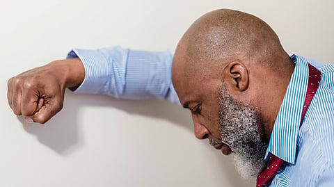 A stressed man leans against a wall with his head down.