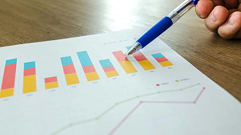 A hand holding a pen points to a graph on paper.