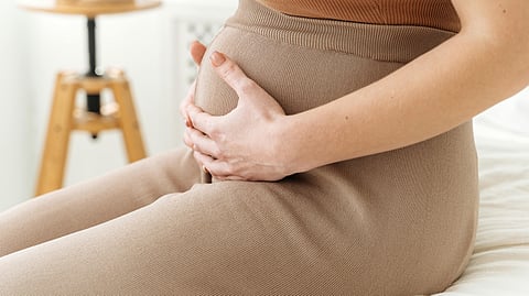 Pregnant woman holding her abdomen with both hands in a gesture associated with pregnancy discomfort or maternal health concerns.