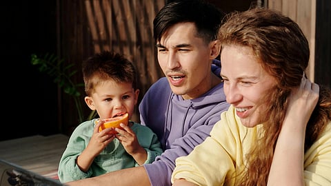 A man, woman and child seated at a wooden table, engaged in conversation.
