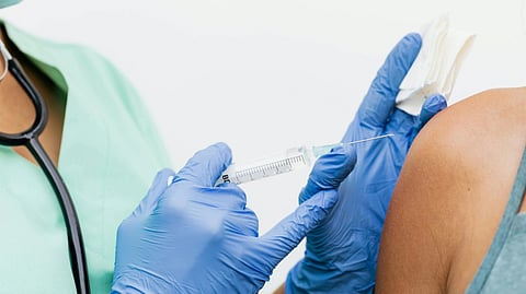 A healthcare worker administers an injection into a patient's upper arm.