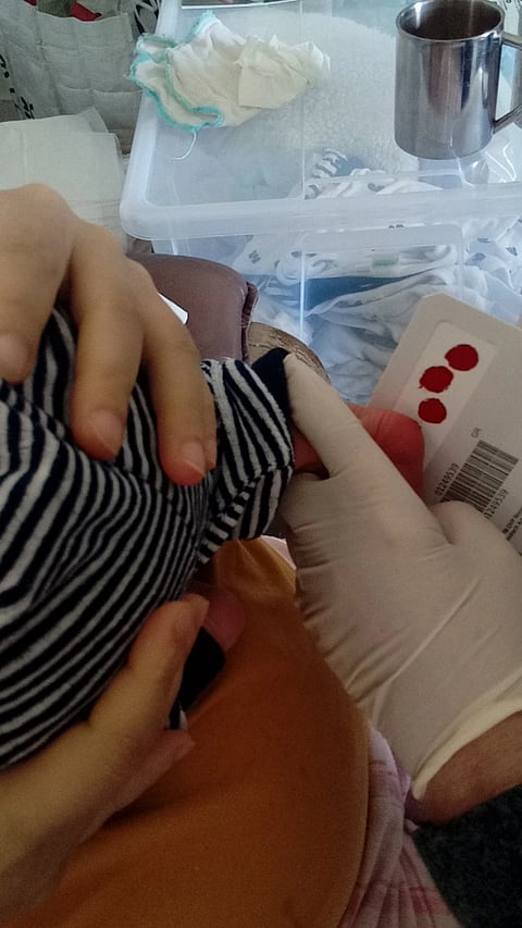 Healthcare worker collecting a dried blood spot sample from a newborn for screening of immunodeficiency disorders.