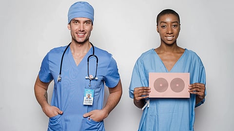 Two healthcare professionals in blue scrubs stand against a light background. 