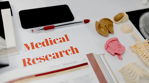 Desk with medical research papers, anatomy models, pen, phone, and open book showing a study setup.