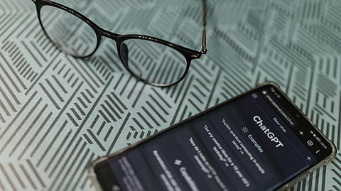A smartphone and a pair of glasses resting on a wooden table surface.
