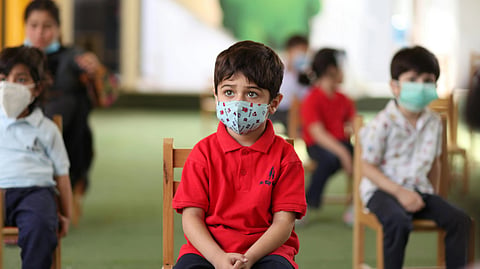 Children wearing masks sit attentively in a classroom.