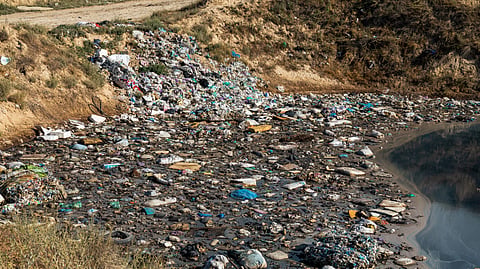 A polluted waterway is filled with trash and debris, surrounded by dry, eroded earth.