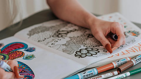 A colouring book, colours and a hand on the book.