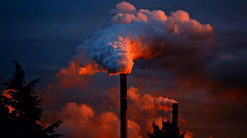 Tall smokestacks releasing white smoke into the evening sky.