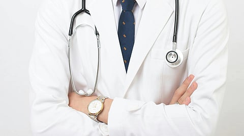 A doctor with hands folded and stethoscope around neck.