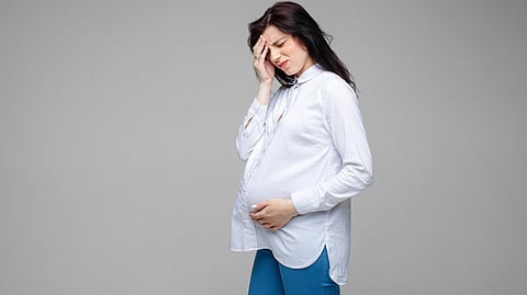 A pregnant woman sits with her head in her hands, expressing a moment of stress or concern.