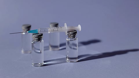 A syringe with a needle positioned next to three vials.