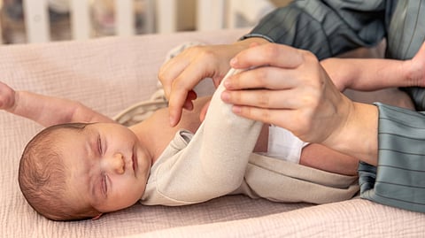 A parent gently changes a sleeping baby's clothes on a soft, beige changing pad.