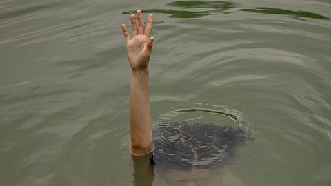 A person floats in water, raising one hand above the surface.