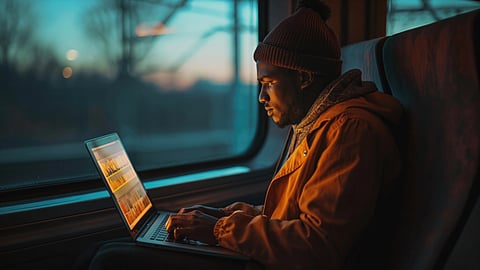 A person wearing a warm jacket and beanie works on a laptop with focus, sitting on a train.