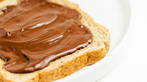Two slices of bread topped with chocolate spread on a white plate.