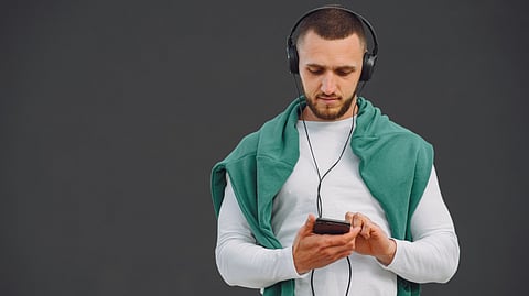 A man wearing headphones looks at his phone.