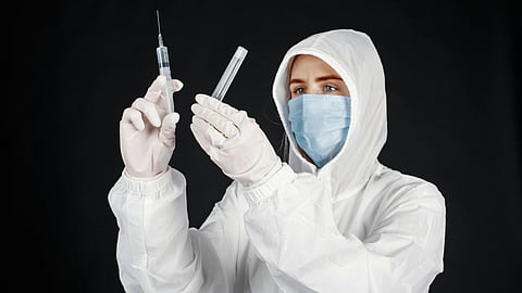 A man in a white coat and mask holds a syringe.