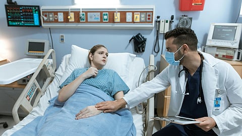 A doctor talks with a patient in a hospital bed about their treatment and care.