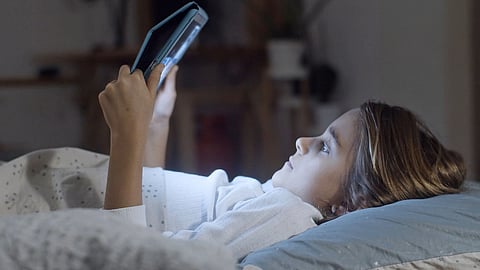 A child lies in bed using a tablet at night.