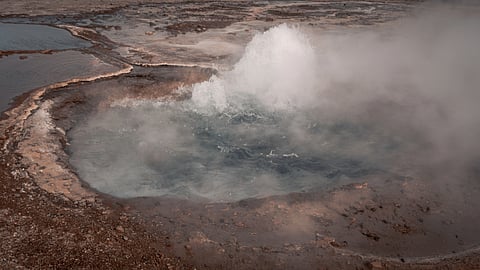 Steaming geothermal pool surrounded by volcanic rock, representing the early Earth environment proposed for RNA self-replication